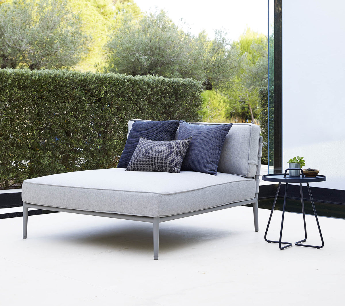 Fauteuil lounge gris élégant avec des coussins bleu marine à côté d'une petite table d'appoint noire dans un cadre serein.