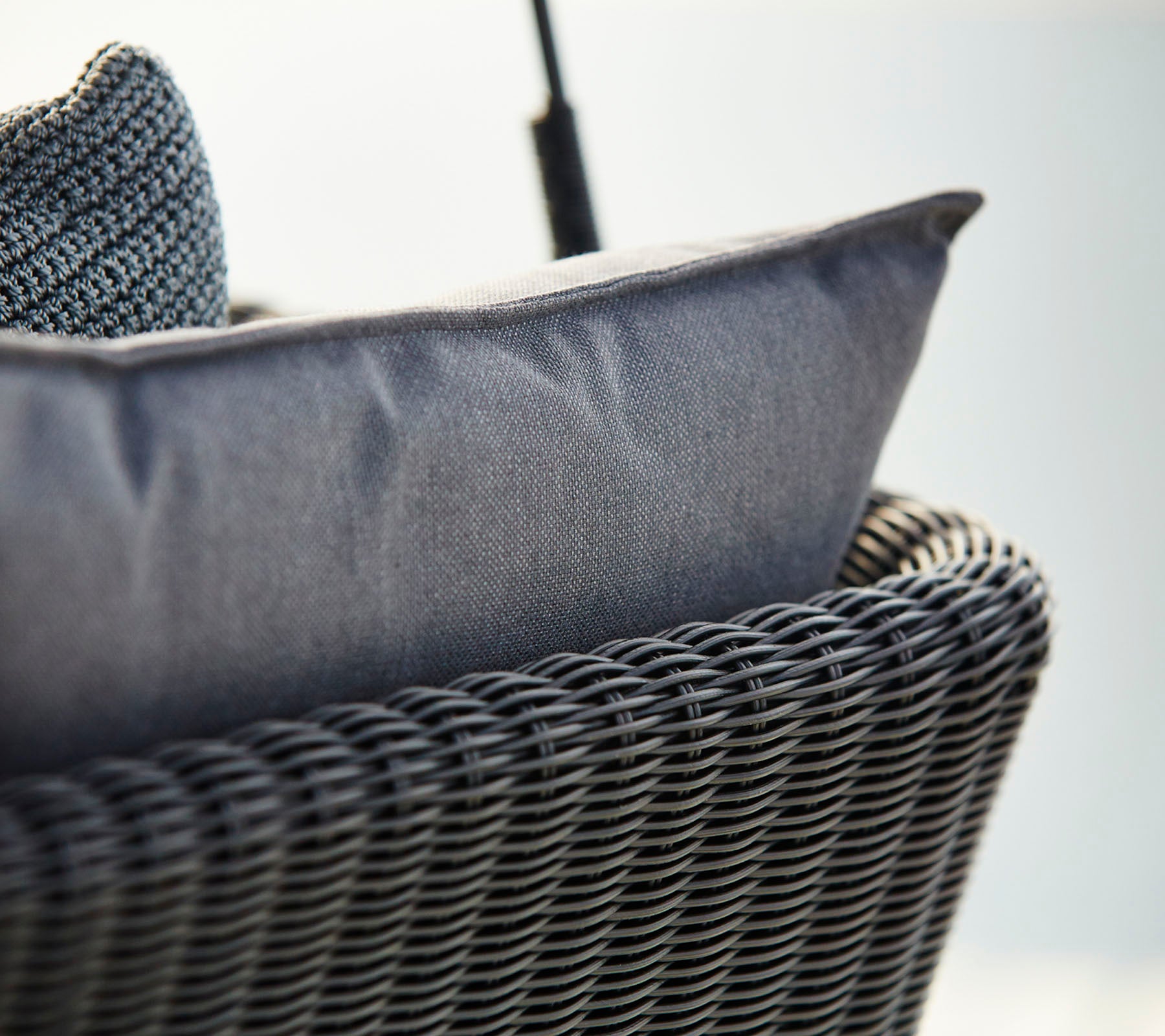 Gros plan d'une chaise en osier avec un coussin texturé gris foncé, mettant en avant le confort et le design moderne.