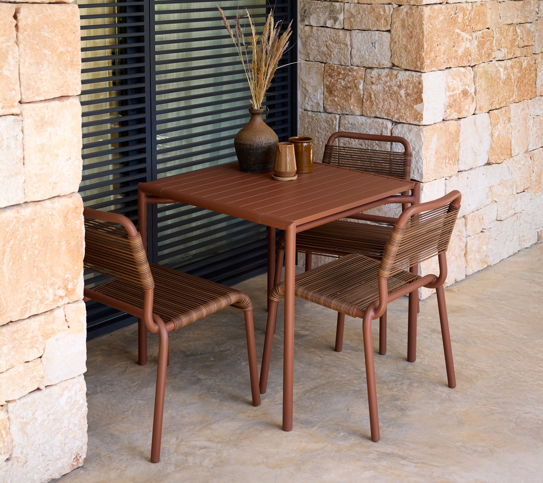 Table et chaises brunes dans un cadre extérieur moderne avec des murs en pierre.