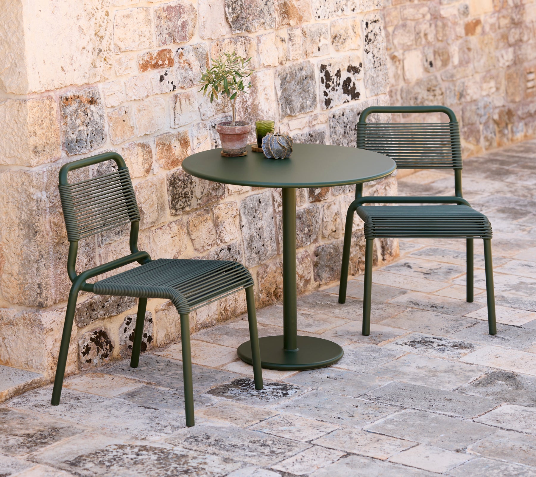 Deux chaises vertes et une table ronde verte dans un cadre extérieur.