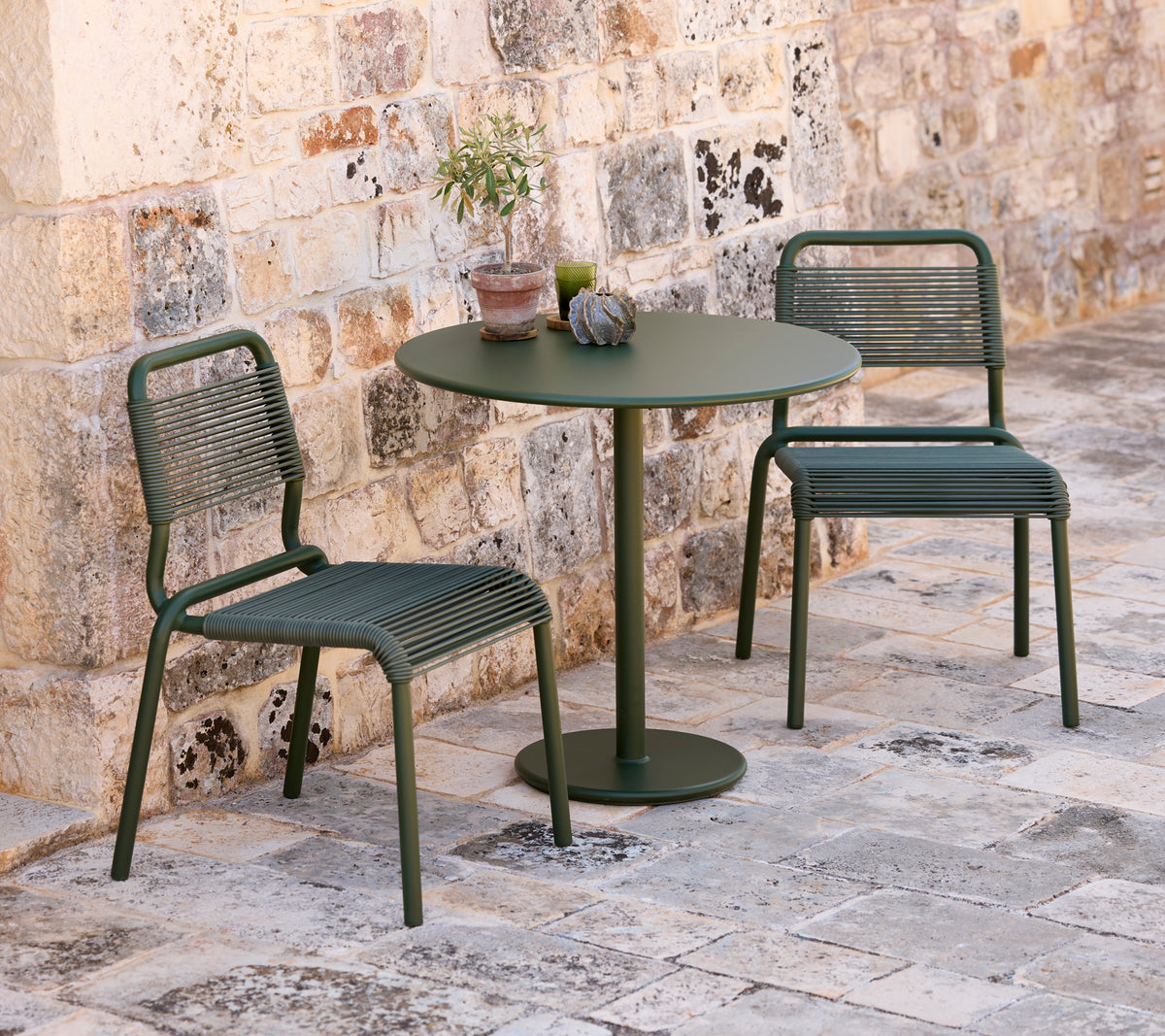 Deux chaises vertes et une table ronde verte dans un cadre extérieur.