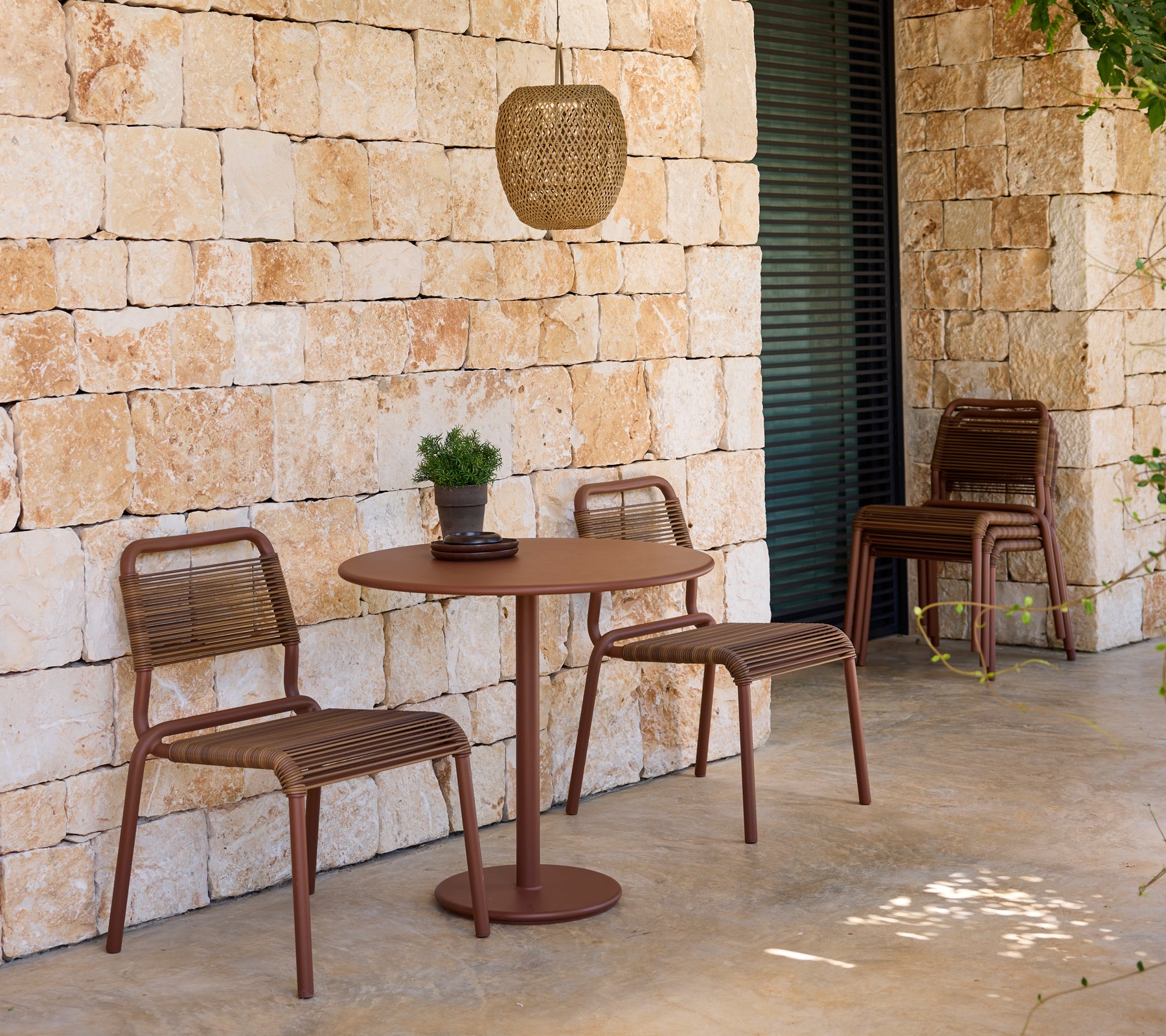 Sièges d'extérieur modernes avec des chaises et une table brunes contre un mur en pierre.