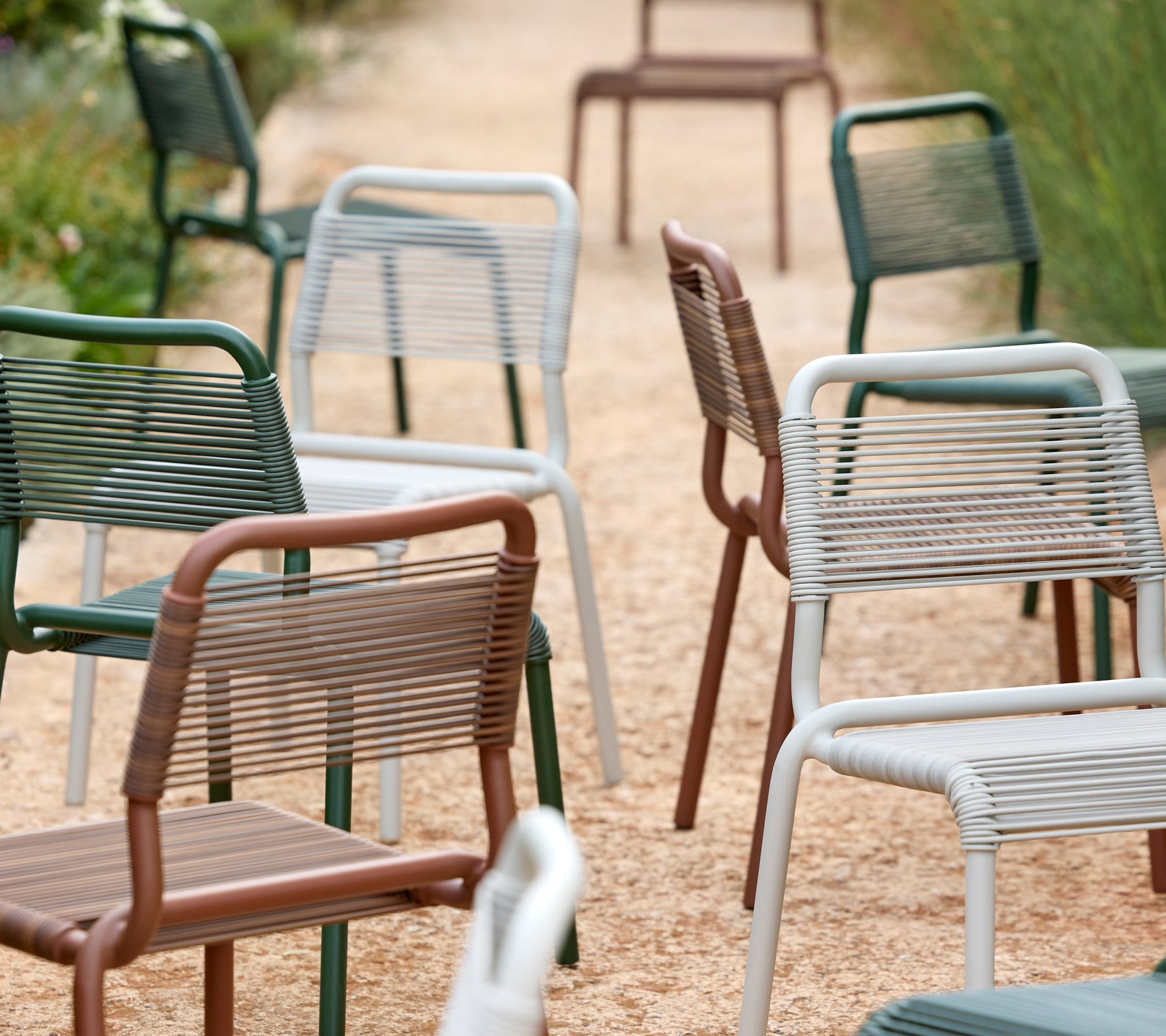 Une gamme de chaises modernes en vert, gris, marron et blanc sur un chemin en gravier.