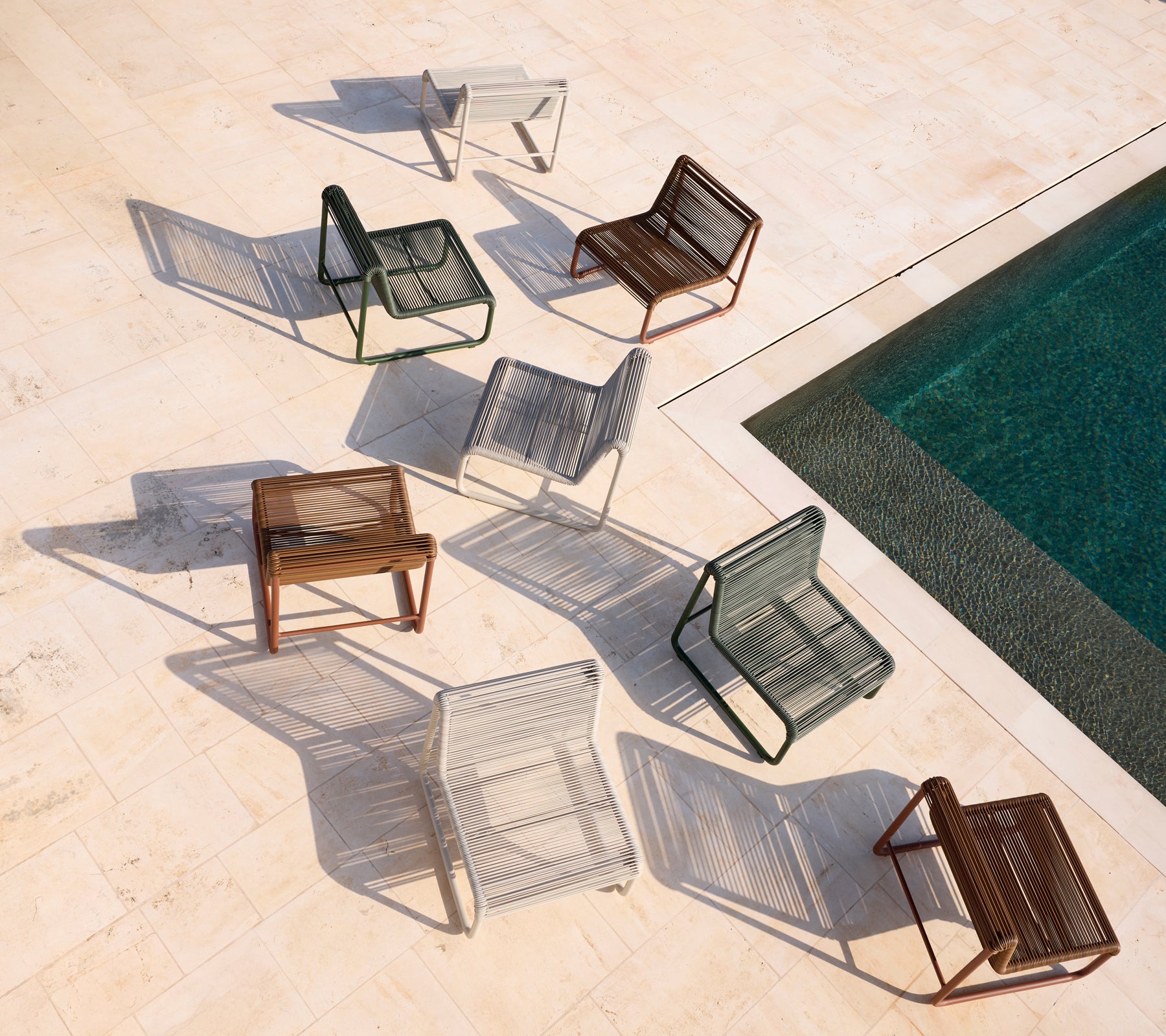 Assortiment de chaises modernes en marron, gris, blanc et noir disposées autour d'une piscine.