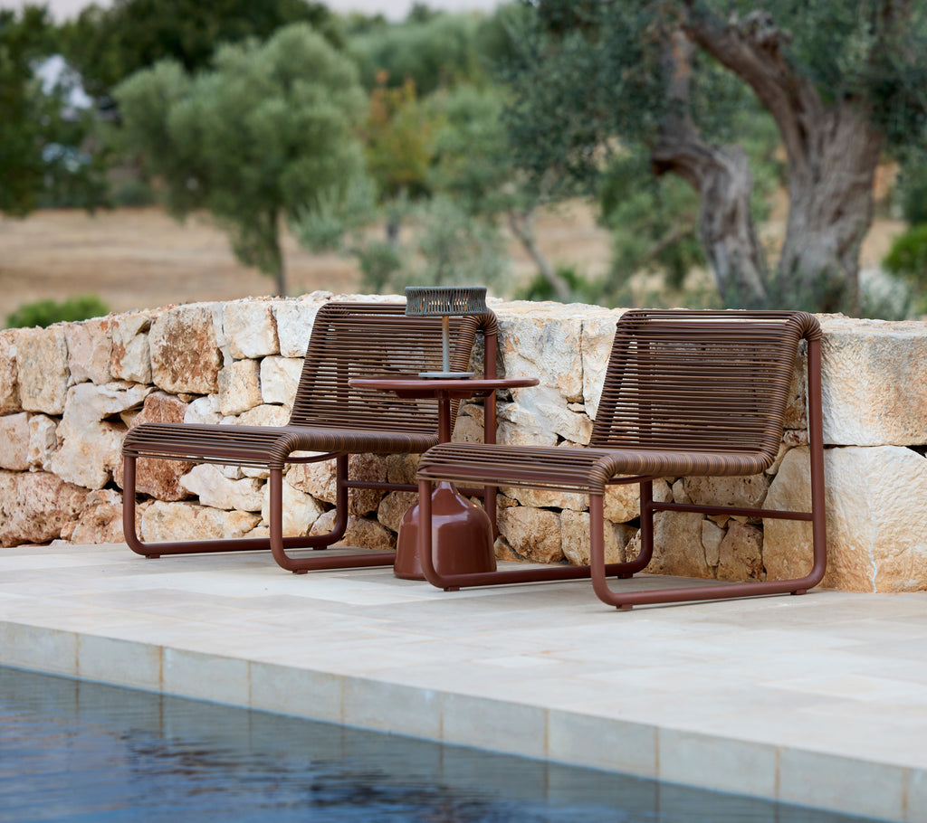 Deux fauteuils modernes marron avec une table d'appoint assortie au bord d'une piscine.
