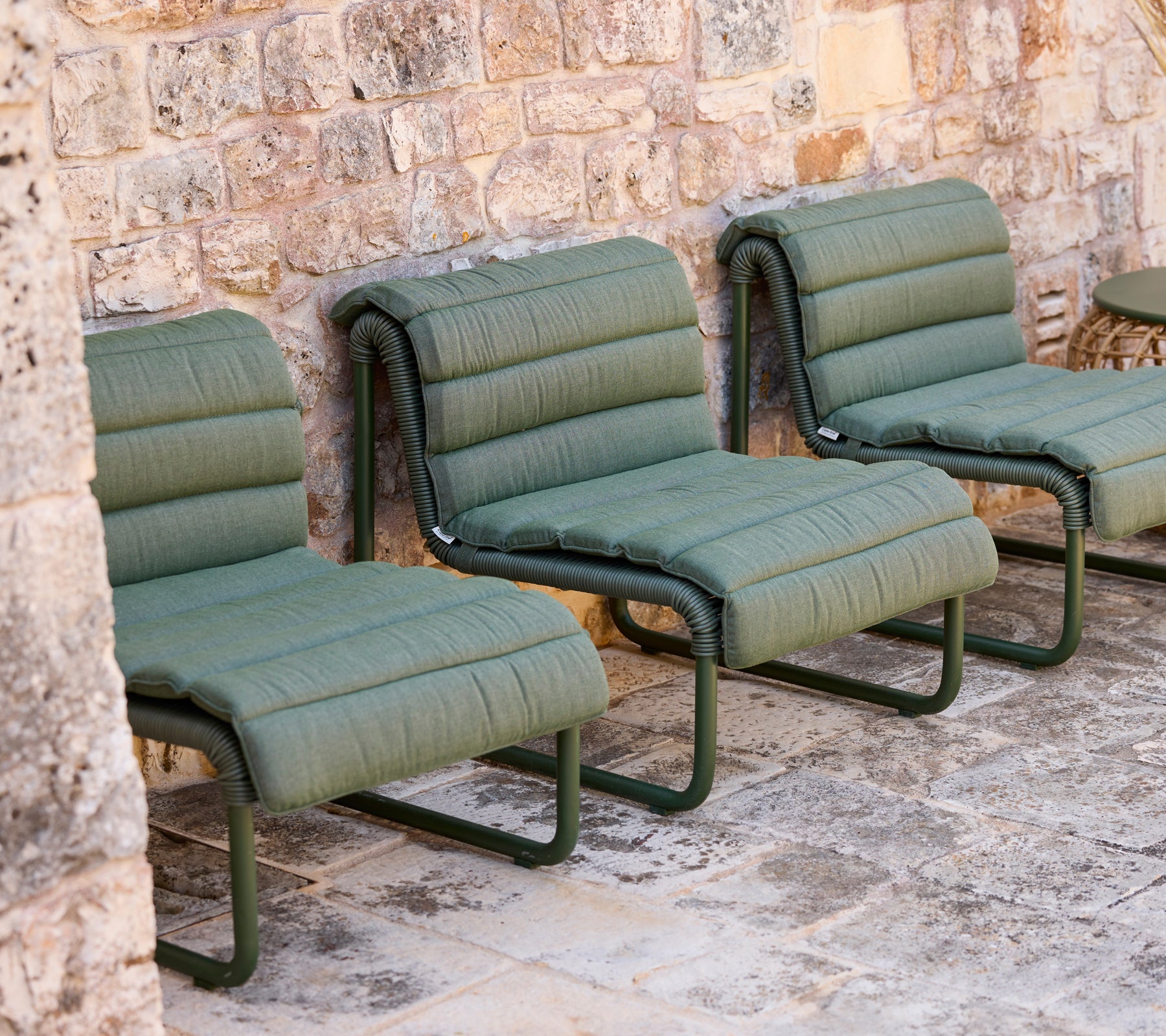 Des chaises longues vertes disposées contre un mur en pierre.