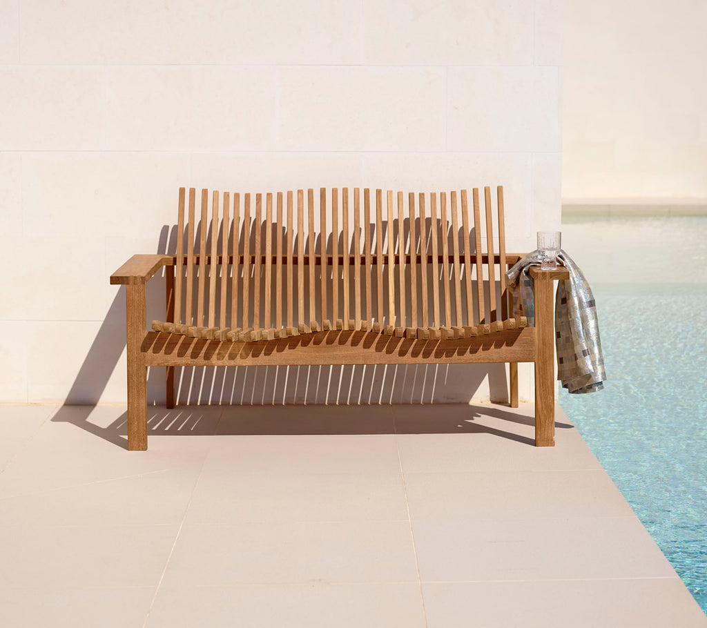 Canapé en bois stylé pour deux personnes avec un design à lattes, complété par un plaid douillet, à côté d'une piscine tranquille. Parfait pour la détente.