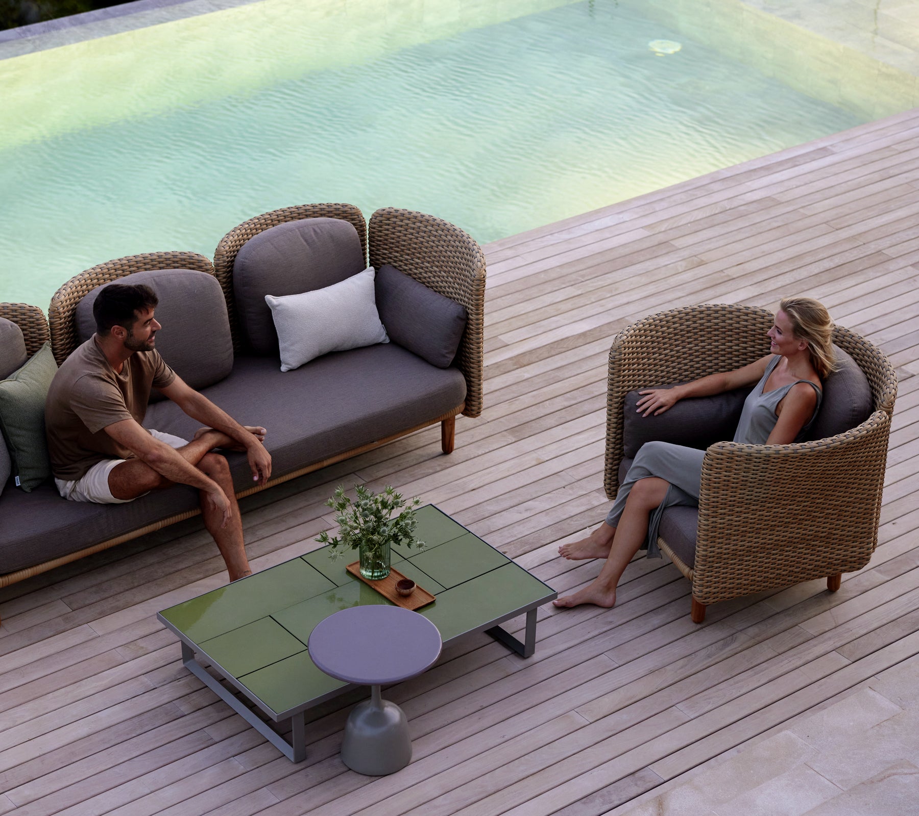 Deux personnes assises dans des fauteuils confortables autour d'une table basse élégante, avec une fontaine tranquille en arrière-plan.