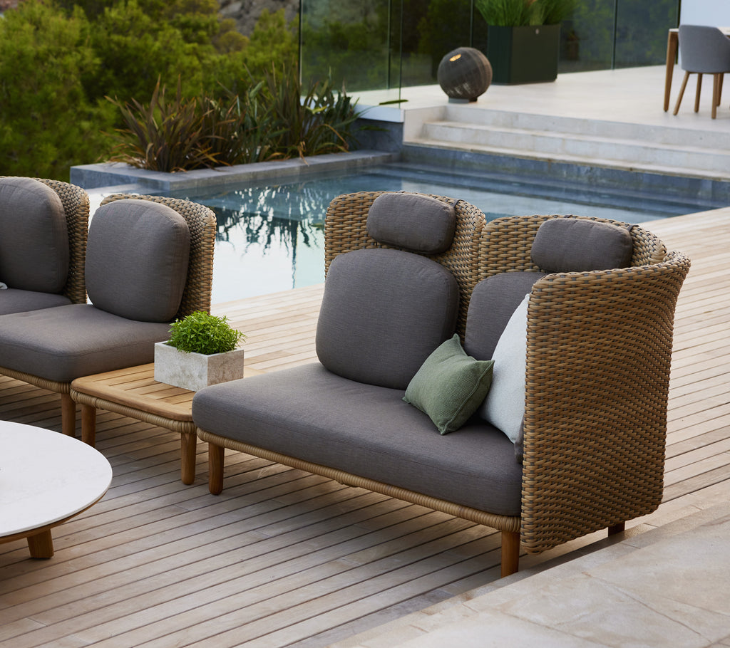Canapé élégant avec un dossier haut et des accoudoirs arqués, featuring des coussins gris et un mélange de coussins décoratifs sur une terrasse en bois.