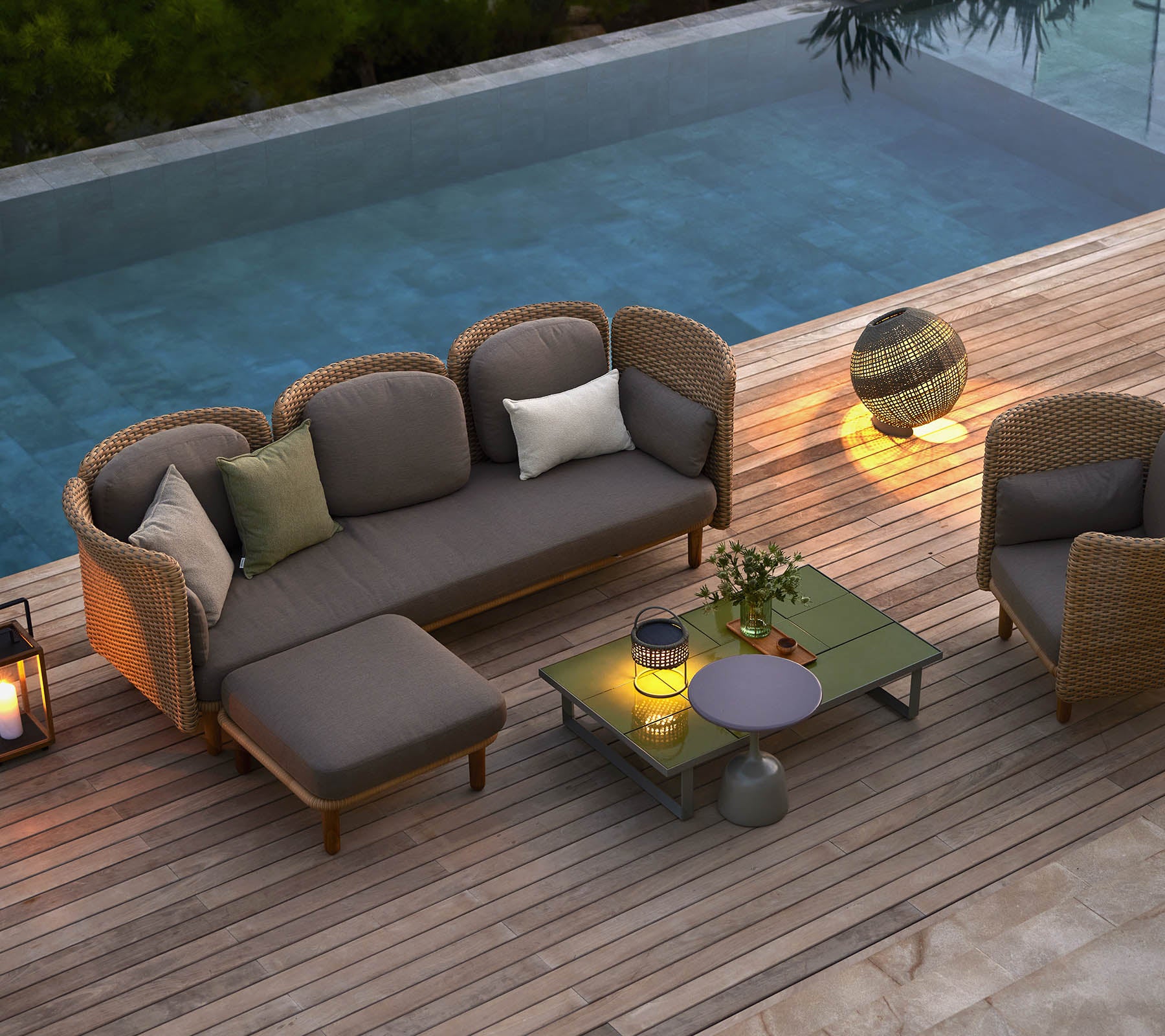 Mobilier de salon élégant avec des coussins, une table basse et un éclairage d'ambiance, situé à côté d'une piscine sereine.
