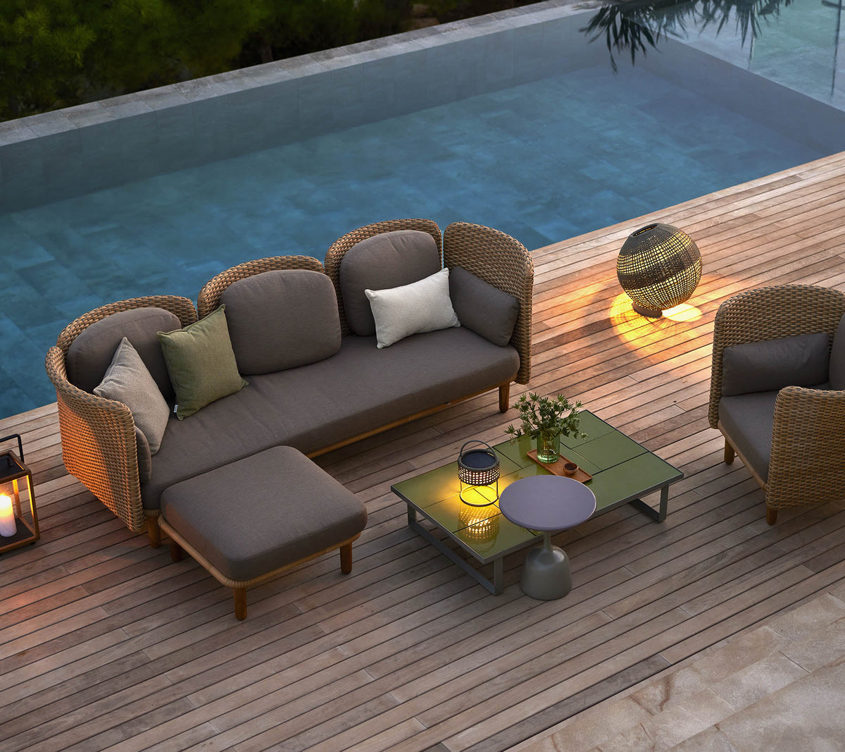 Mobilier de salon élégant avec des coussins, une table basse et un éclairage d'ambiance, situé à côté d'une piscine sereine.