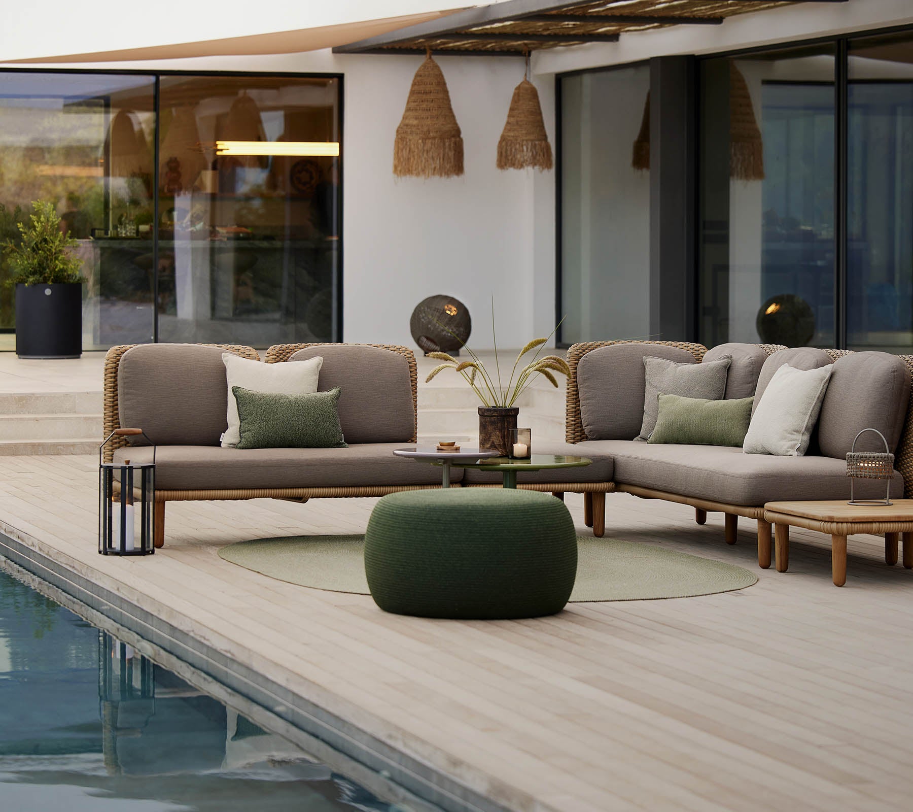 Un espace lounge élégant avec un canapé sectionnel et des coussins, une table ronde et un pouf confortable, situé à côté d'une piscine tranquille.