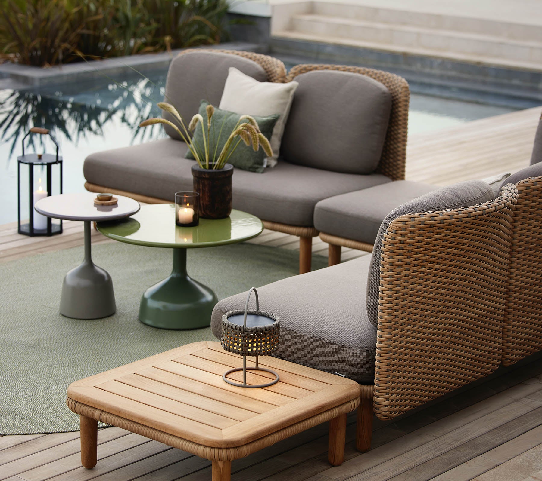 Un espace lounge élégant avec un canapé gris à accents en osier, une table d'appoint verte et des accessoires décoratifs.