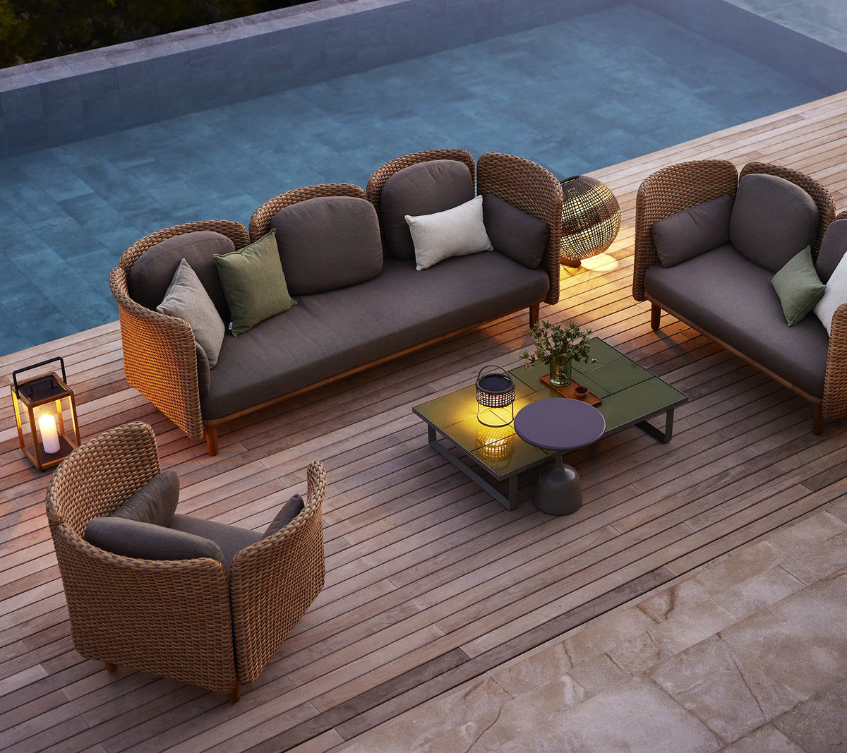 Un aménagement de sièges confortable avec un canapé et des chaises avec des coussins, entouré de verdure et d'une piscine, sur une terrasse en bois.