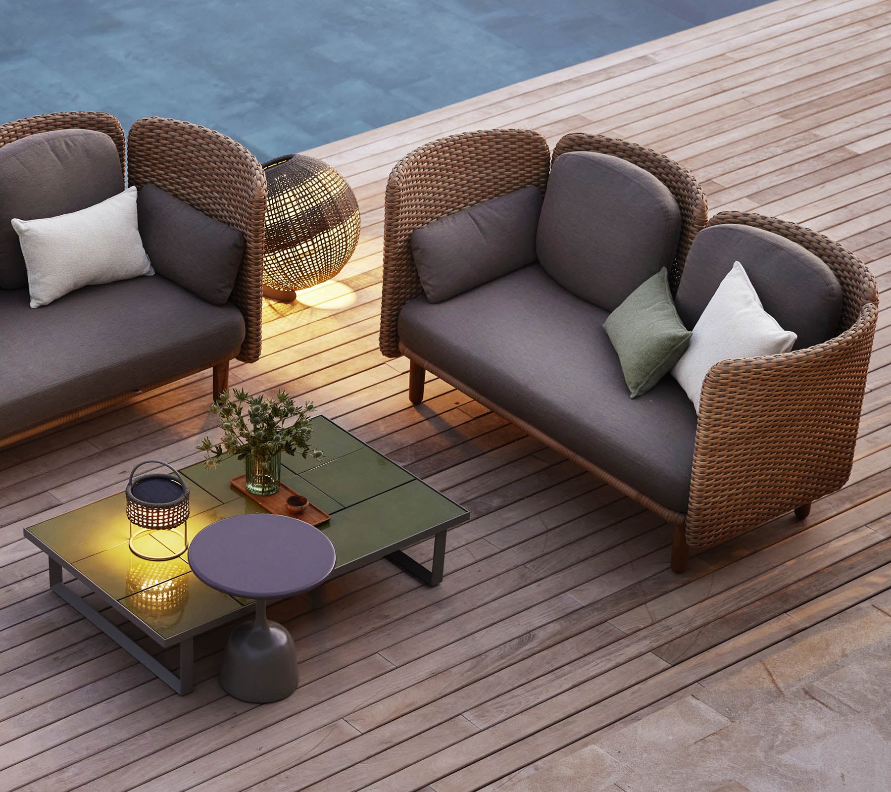 Un coin salon confortable avec deux canapés lounge incurvés, une table basse, des coussins décoratifs et un éclairage d'ambiance.