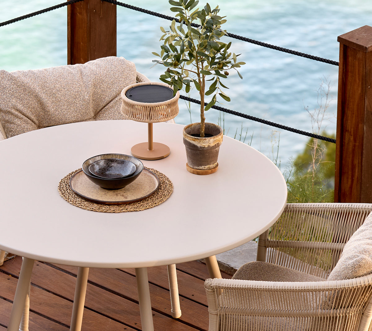 Table ronde blanche avec des chaises tressées, une plante décorative et un bol noir dans un cadre de salon moderne.