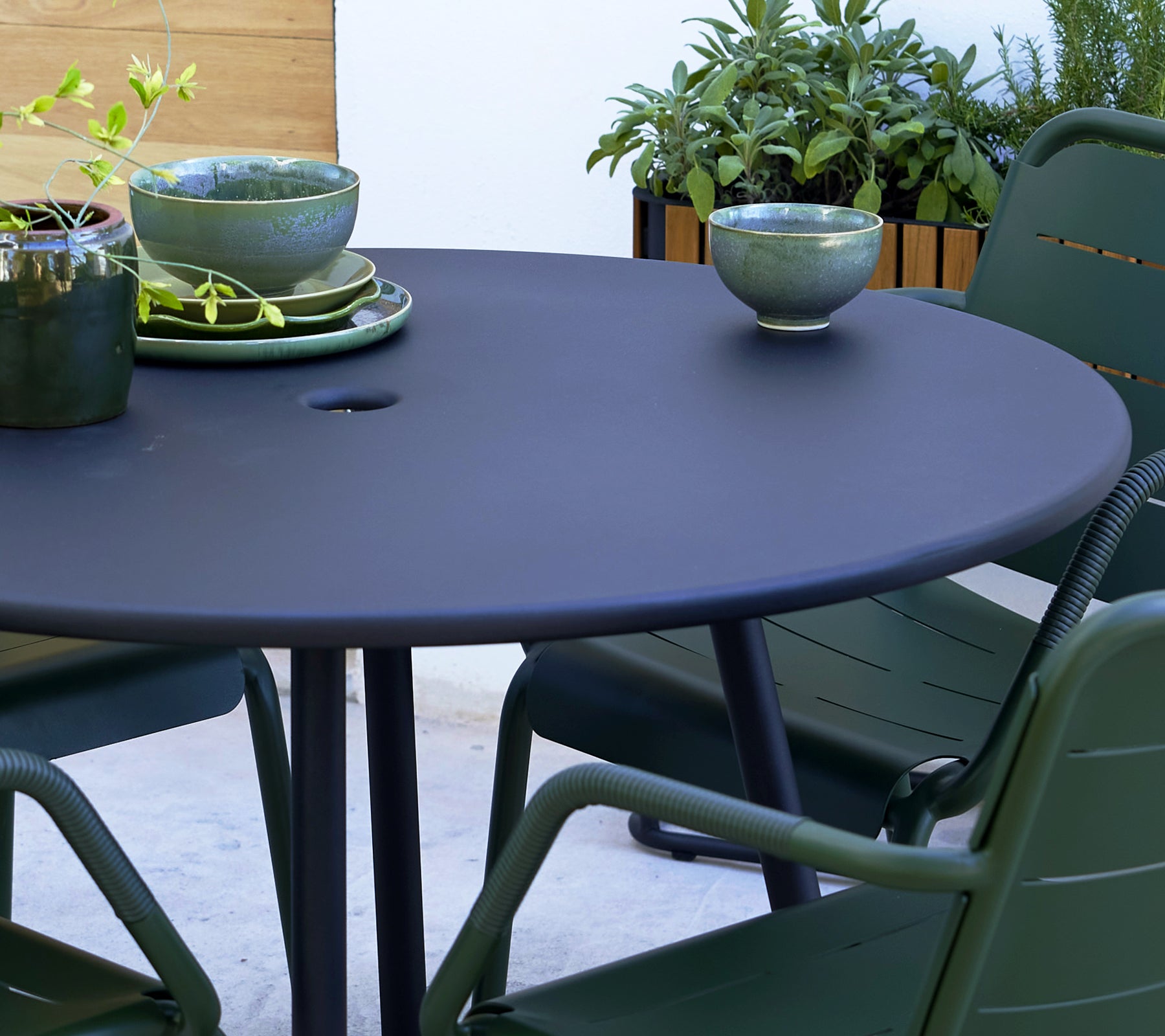 Table ronde grise avec des chaises vertes de Copenhague, ornée de bols décoratifs et de verdure en arrière-plan.