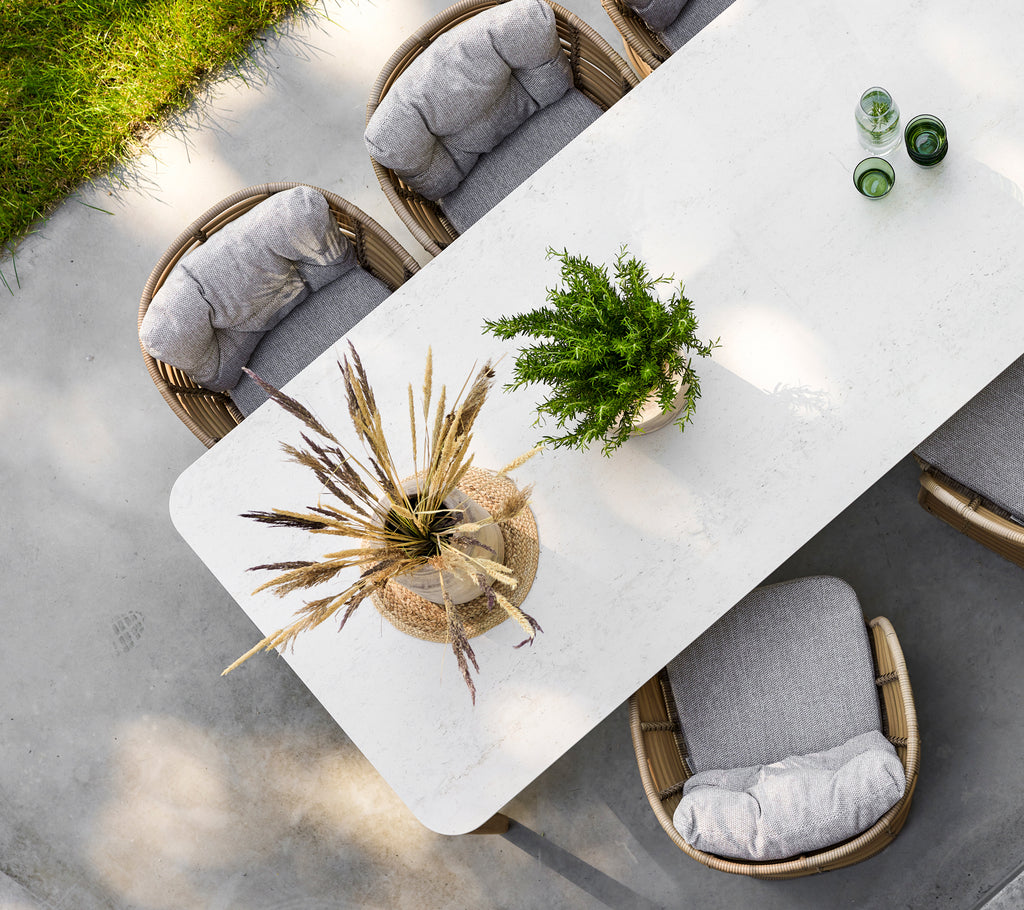 Une table à manger moderne avec une surface texturée, entourée de chaises rembourrées et ornée d'un élégant centre de table végétal.