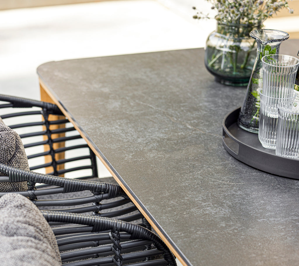 Une configuration de salle à manger moderne avec une table lisse, une chaise en osier élégante, des verres sur un plateau et un vase décoratif avec de la verdure.