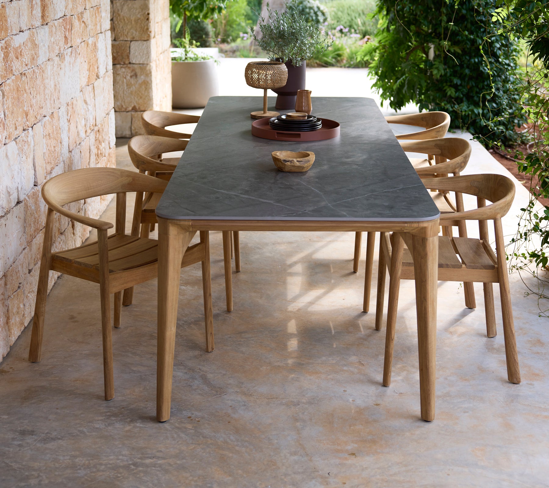Table à manger moderne d'extérieur avec surface noire et chaises en bois dans un cadre naturel.