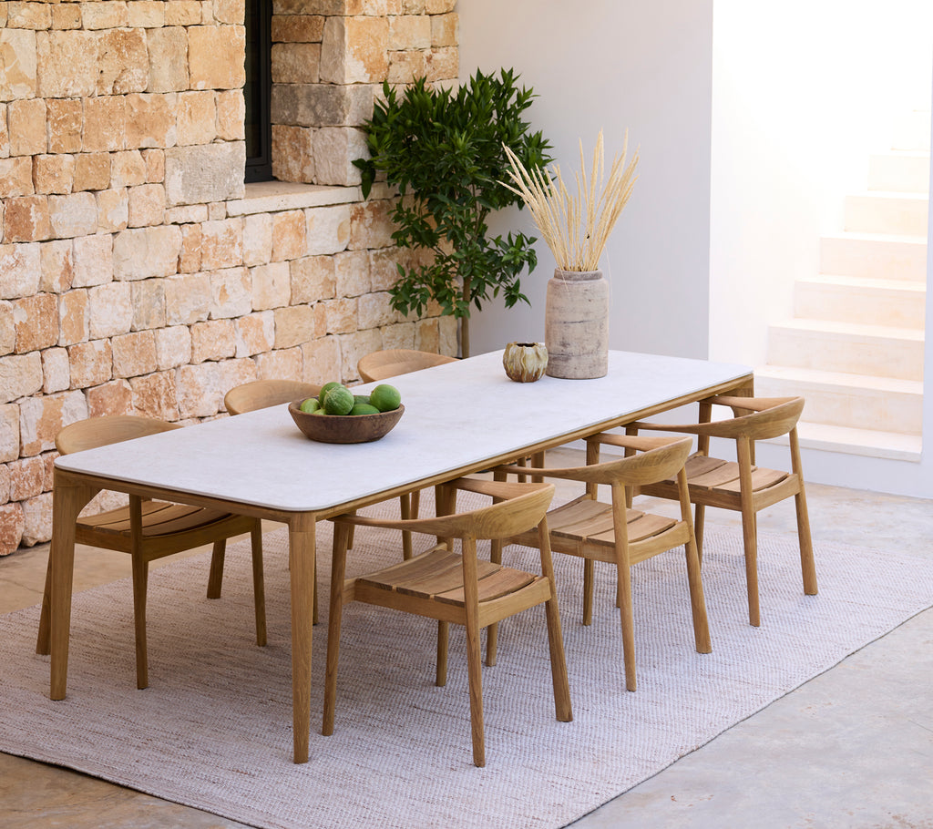Agencement moderne de salle à manger avec une table blanche et des chaises en bois contre un mur en pierre.