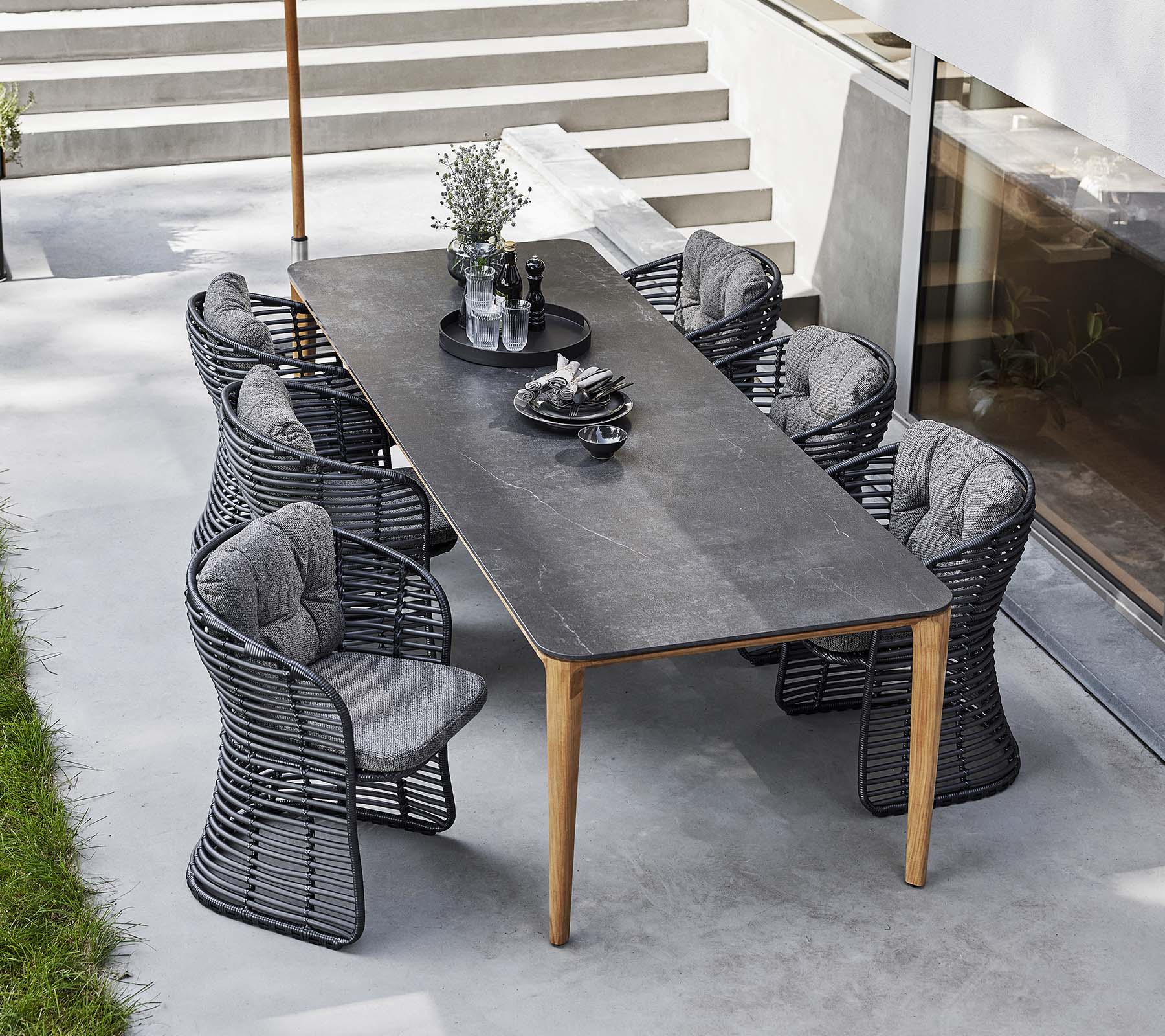 Des chaises en osier entourent une table épurée, complétée par un parasol classique et des centres de table décoratifs pour une mise en place accueillante en plein air.