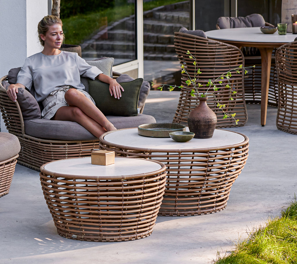 Une personne assise se détend à côté de tables basses en osier de taille moyenne et grande, présentant un mélange de matériaux naturels et un design minimaliste.
