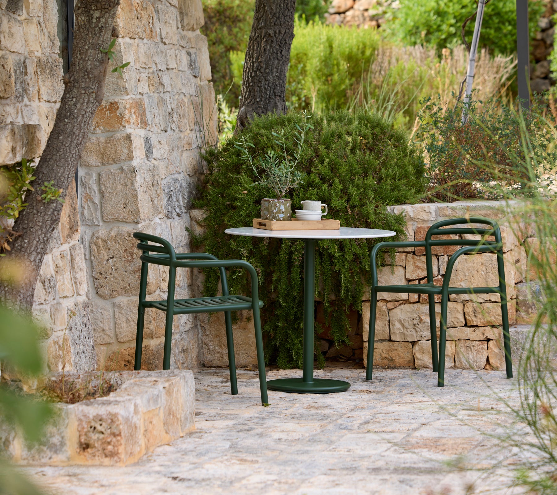 Chaises vertes entourant une table ronde dans un cadre en pierre en extérieur.