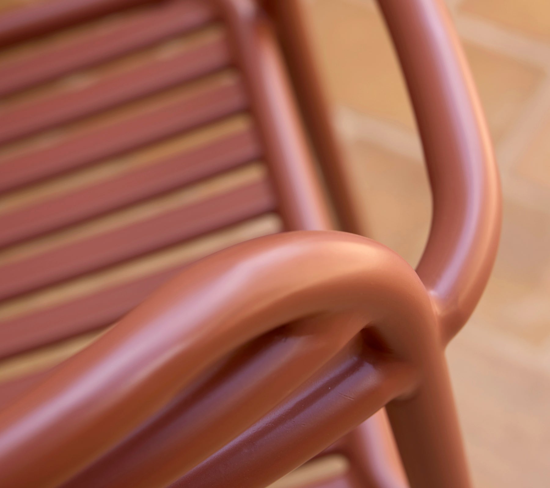 Gros plan d'un fauteuil Bliss dans une teinte rouge désert, mettant en valeur ses courbes lisses et son design à lattes.
