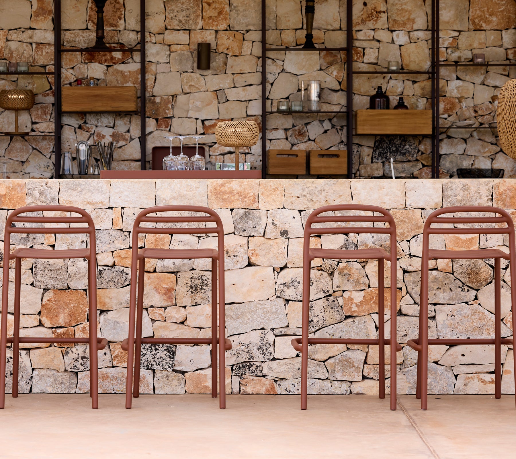 Chaises de bar marron devant un mur en pierre avec des étagères.