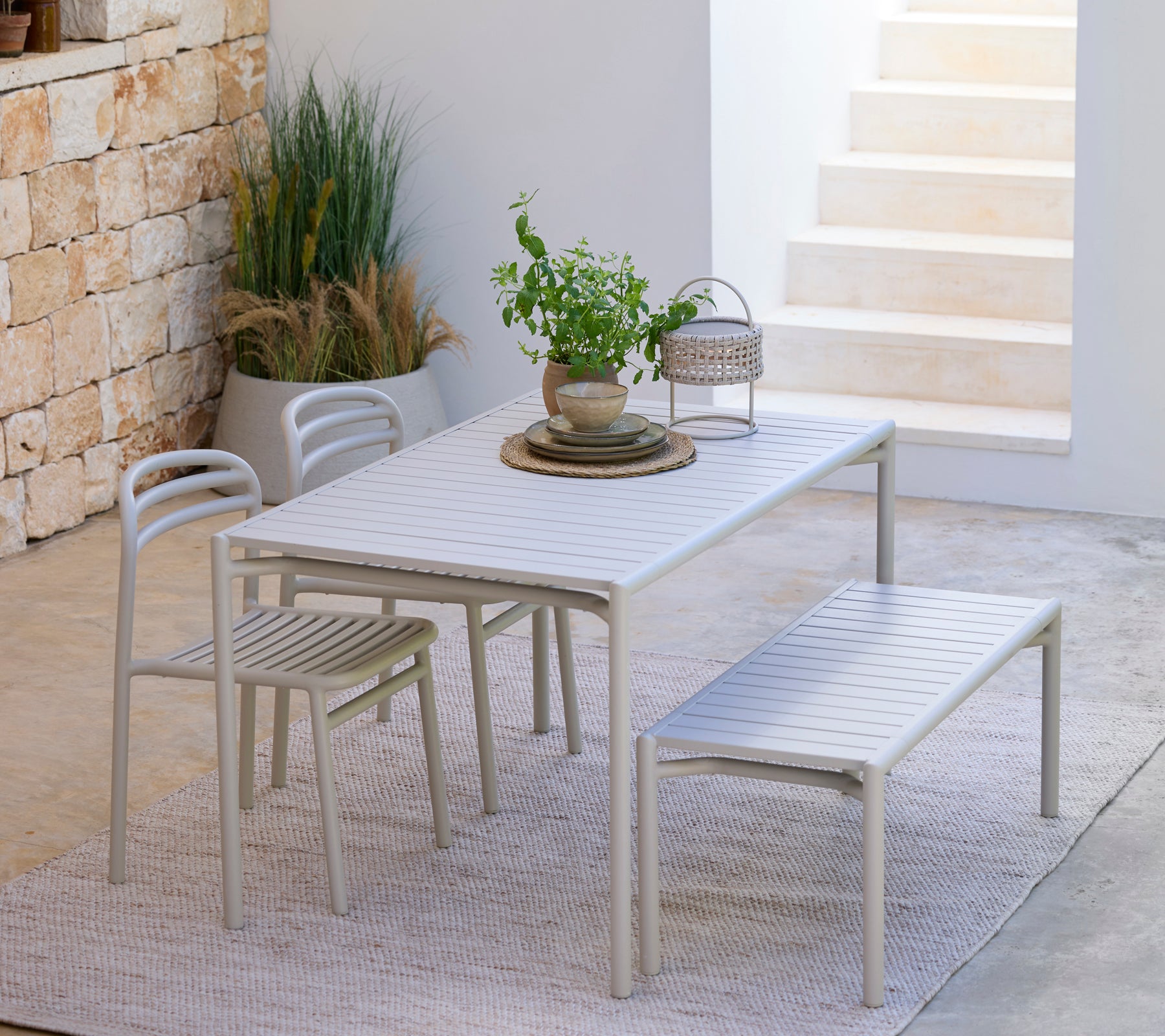 Ensemble de salle à manger gris clair comprenant une table, des chaises et un banc dans un cadre moderne en plein air.
