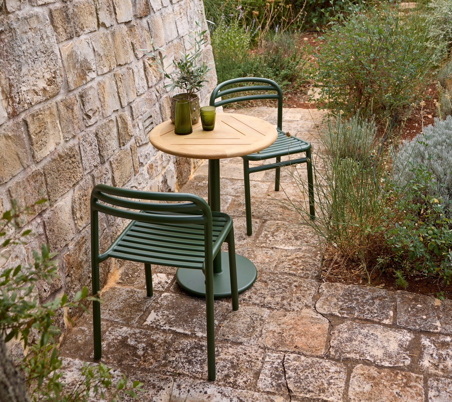 Cadre extérieur avec une chaise verte, une table en bois et un vase en verre.