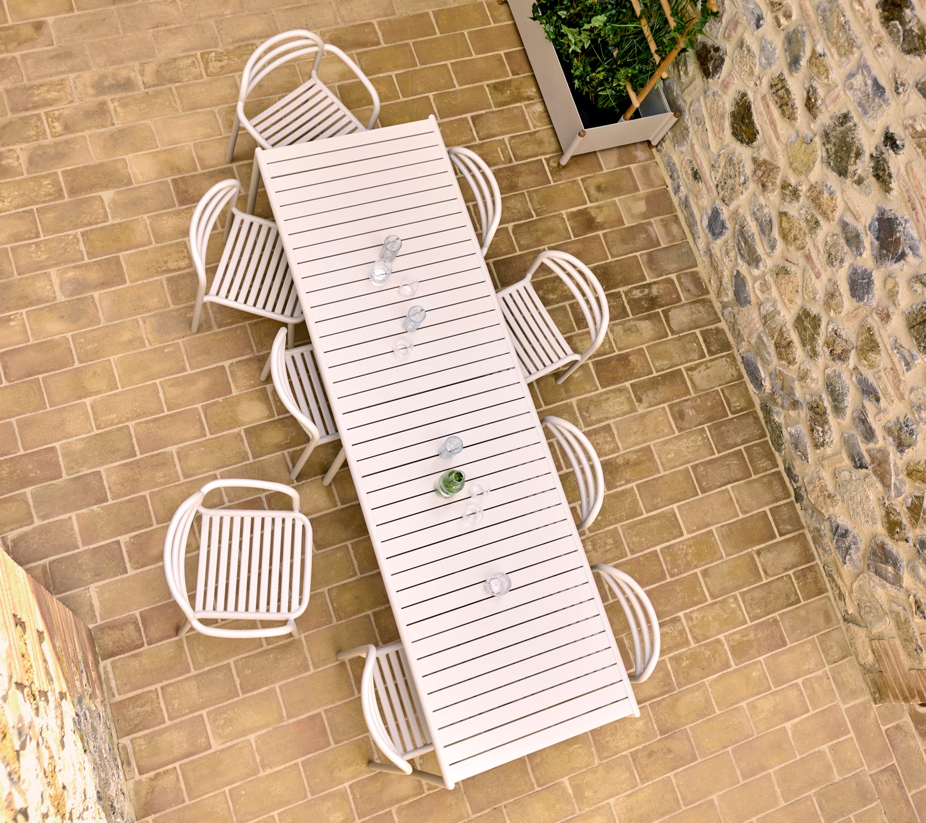 Vue aérienne d'une table à manger d'extérieur de couleur sable avec huit chaises Bliss, située sur une terrasse en pierre.