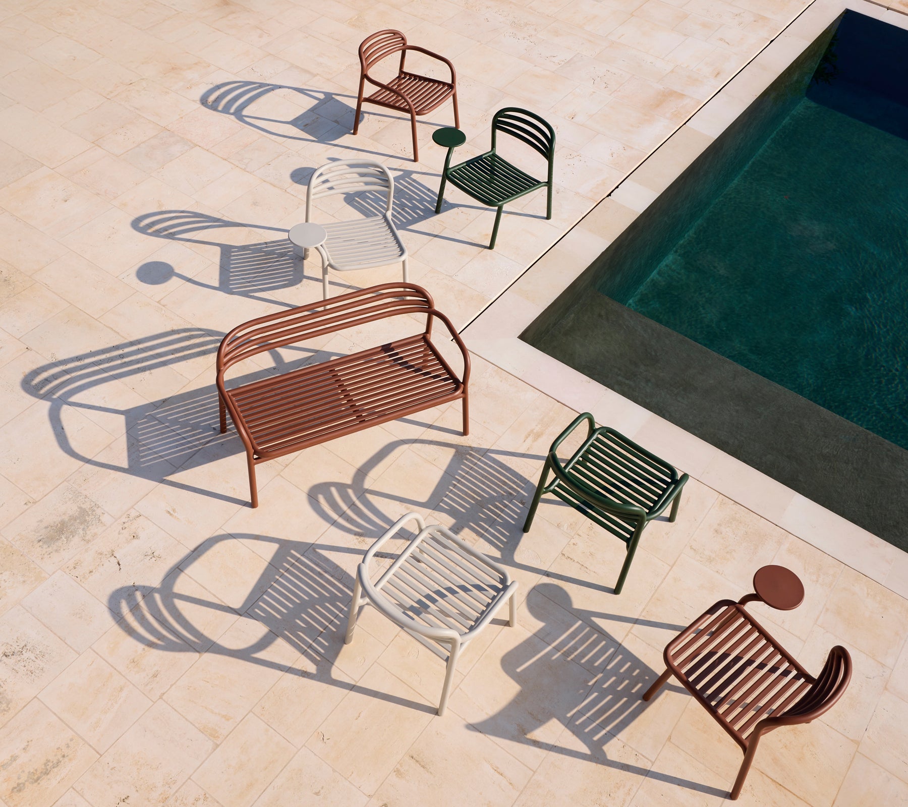 Ensemble de chaises modernes rouges, blanches et vertes et un banc marron près d'une piscine.