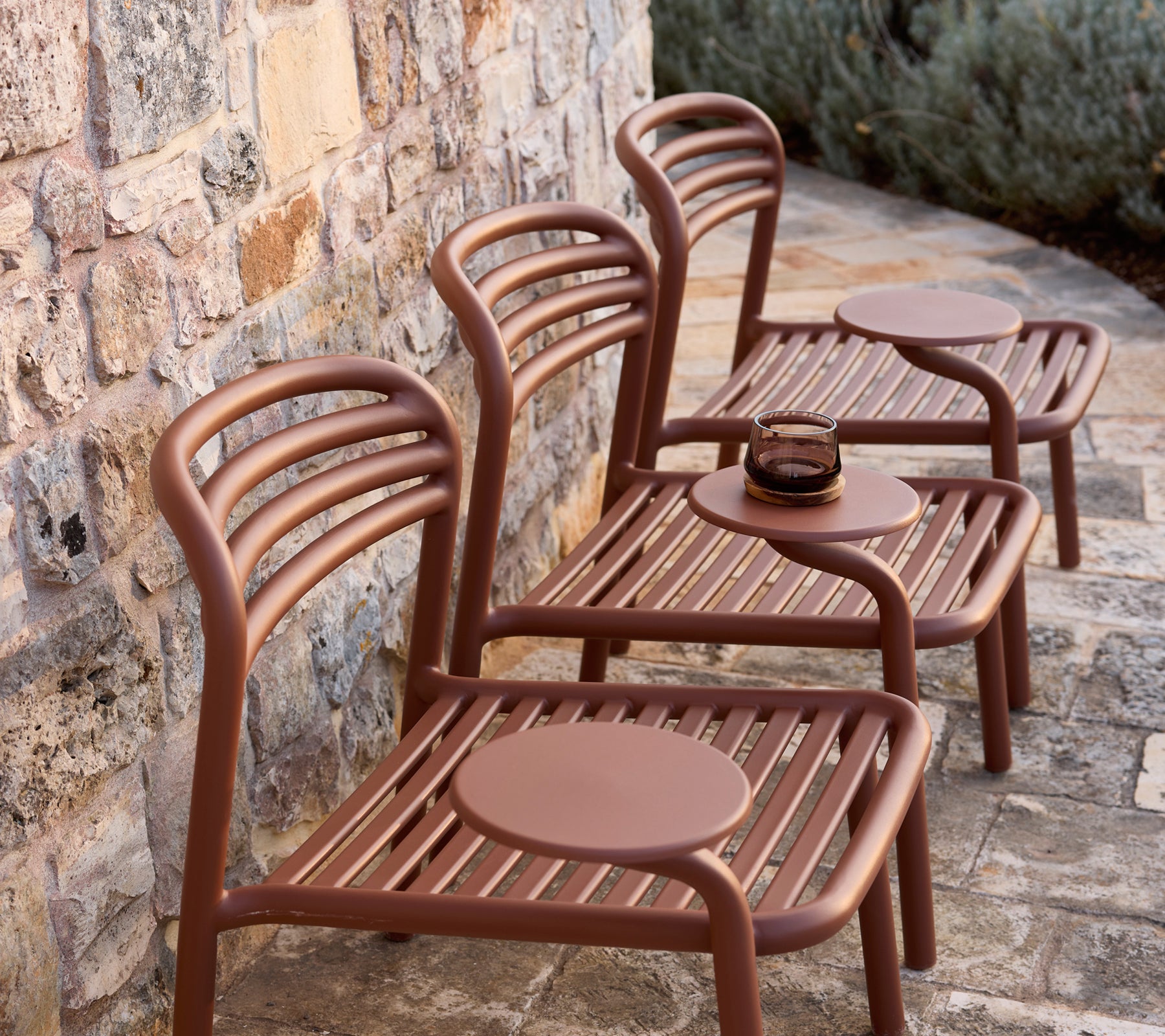 Trois chaises marron modernes avec des tables rondes contre un mur en pierre.