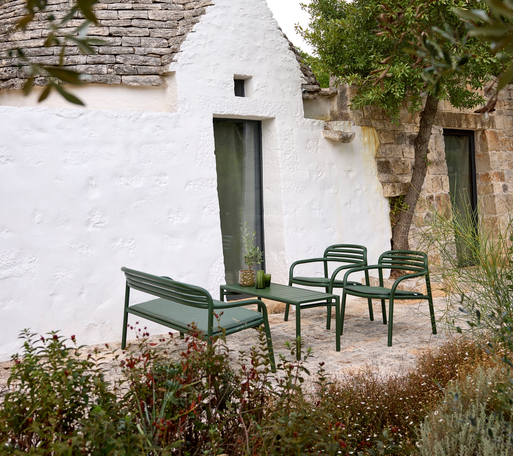 Canapé d'extérieur vert et fauteuils avec une table basse dans un cadre confortable.