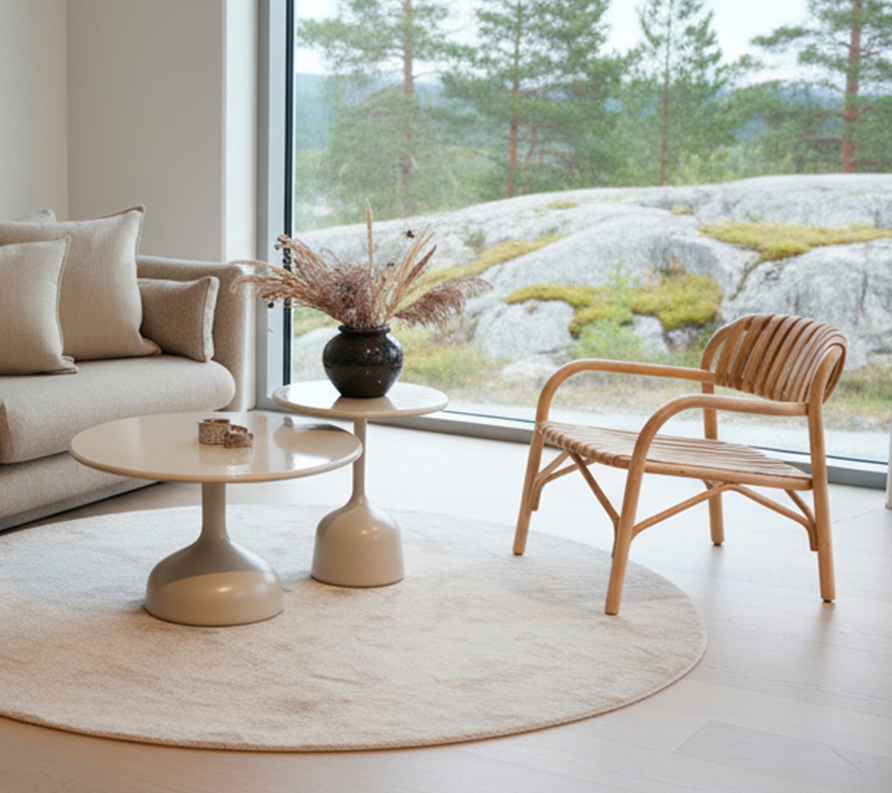 Salon moderne avec un canapé, une table ronde, un vase noire et une chaise en rotin près d’une grande fenêtre.