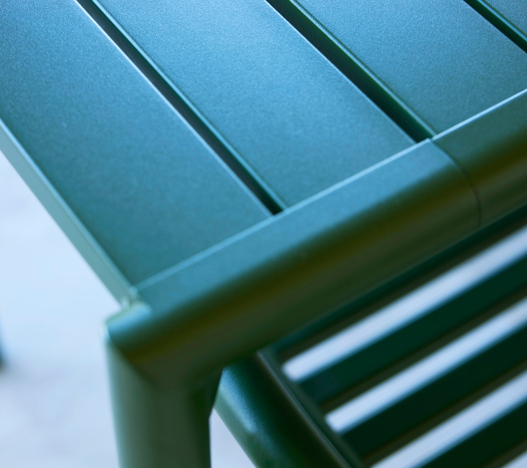 Gros plan d'un coin de table vert avec des lattes horizontales épurées et une finition polie, mettant en valeur un design moderne et une fonctionnalité.