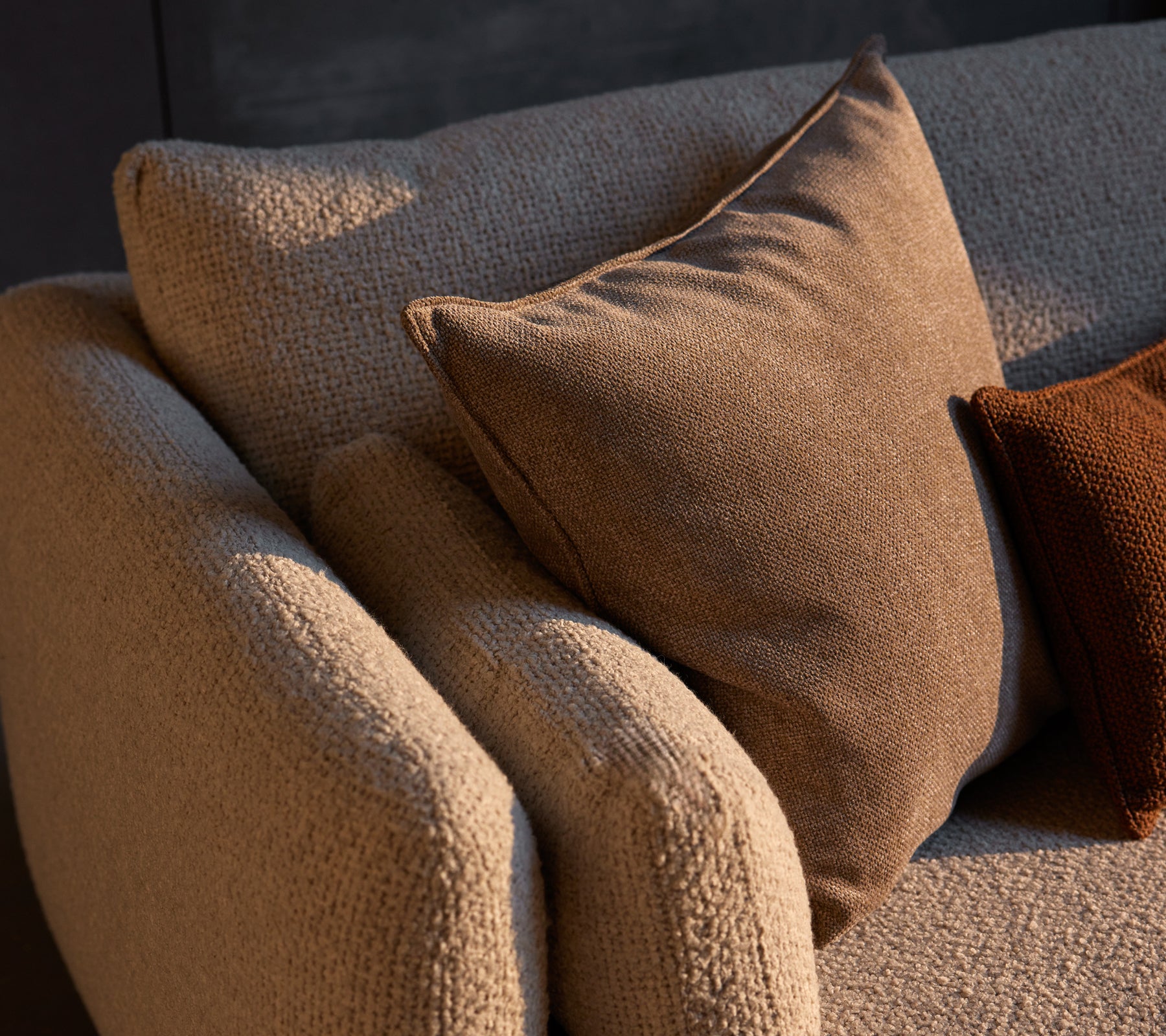Canapé d'angle confortable en tissu texturé avec des coussins Essence dans des tons chauds, ajoutant confort et style à l'espace.