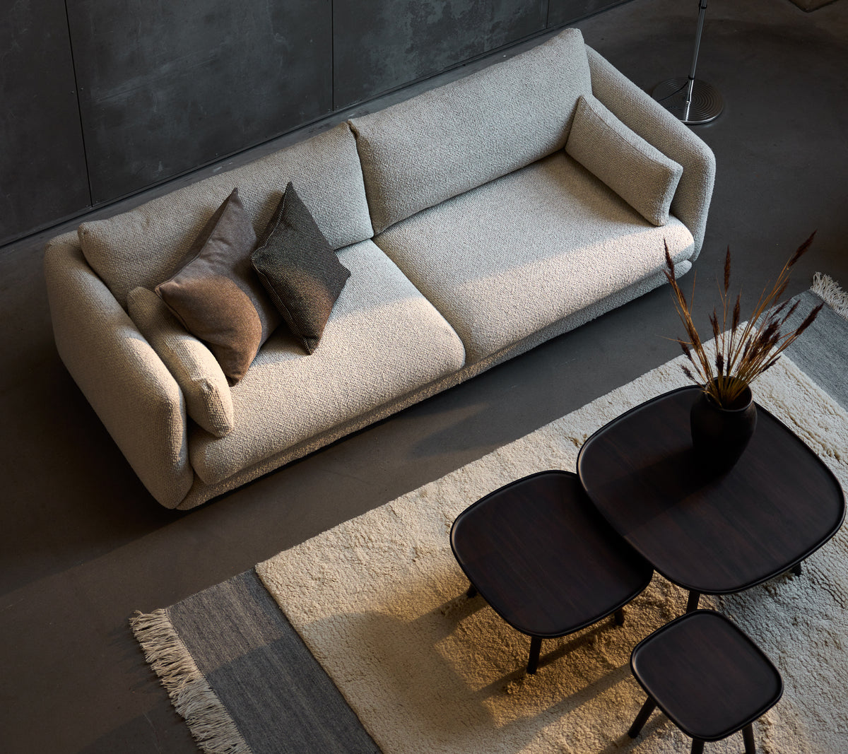 Canapé trois places élégant en couleur sable, complété par trois tailles de tables basses noires élégantes et des coussins décoratifs.