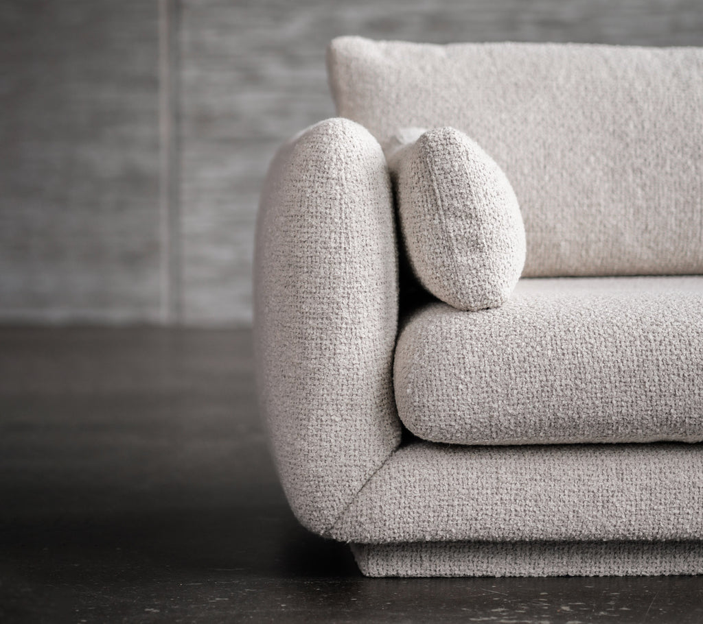 Canapé moderne gris clair avec des accoudoirs arrondis et des détails sur les coussins.