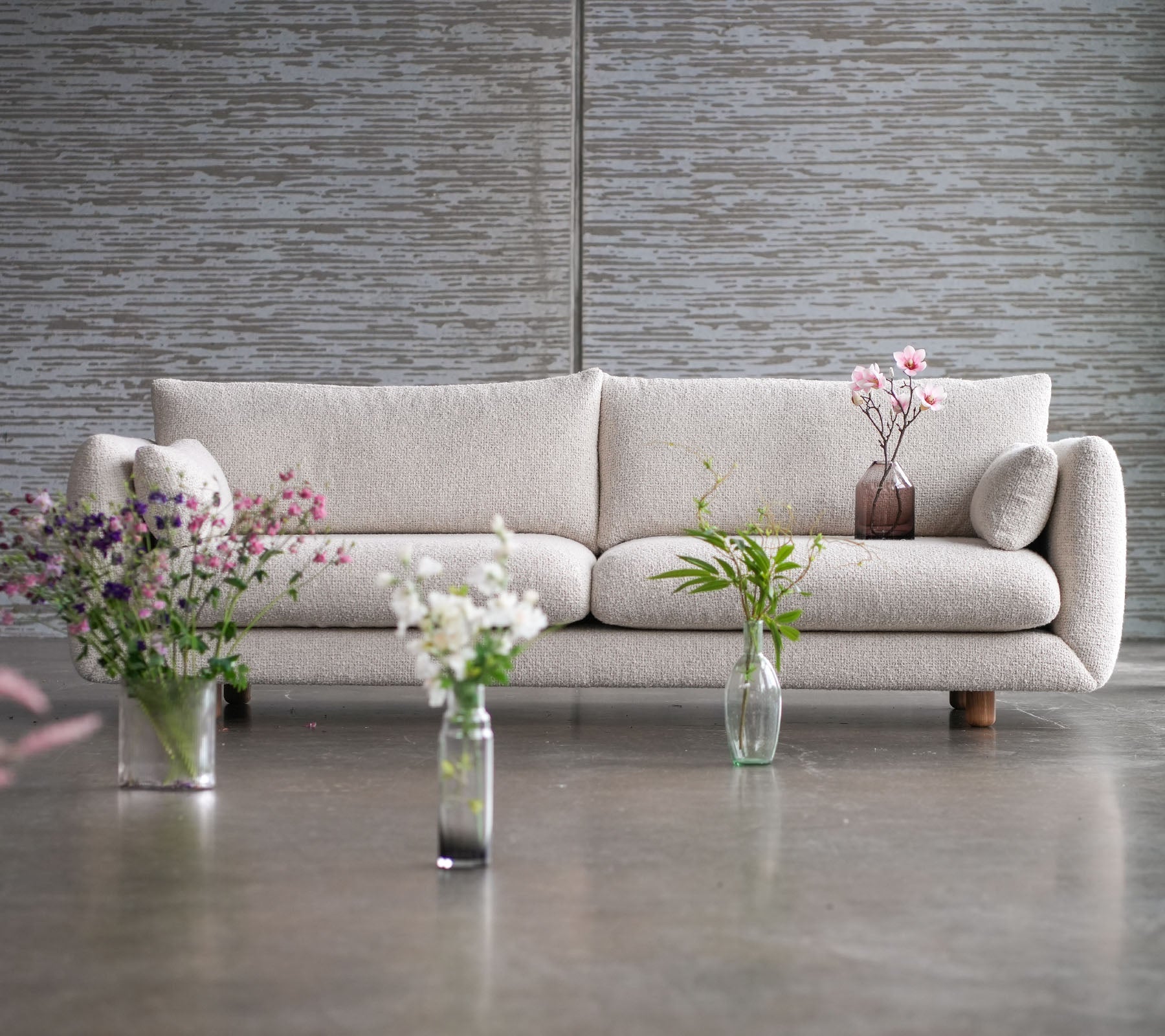 Un canapé de couleur claire avec des pieds en teck, entouré de vases de fleurs, mettant en valeur un mélange d'élégance et de style Cane-line.