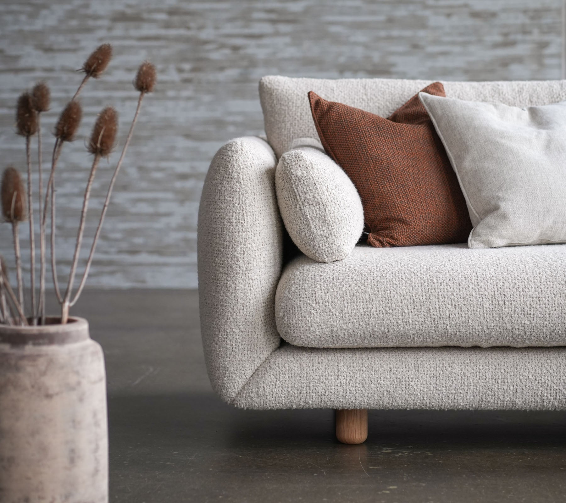 Canapé confortable avec un revêtement fleuri, des pieds en teck et des coussins surélevés, accompagné d'un vase décoratif et de fleurs séchées. Design élégant et accueillant.