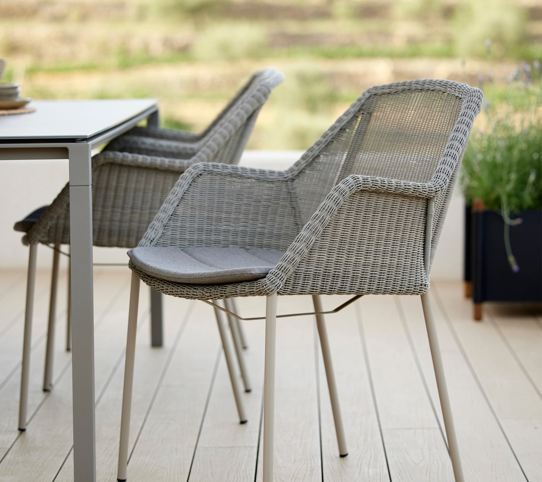 Deux chaises tissées élégantes à côté d'une table moderne, avec un design épuré et des coussins confortables, idéales pour se détendre dans un cadre serein.