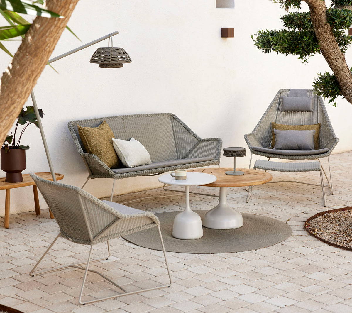 Mobilier de salon élégant avec une table basse, comprenant des coussins texturés et des tons naturels, entouré de verdure et d'un éclairage doux.