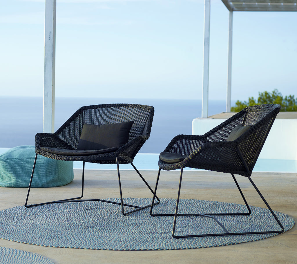 Deux chaises noires modernes avec un coussin bleu sur un tapis rond près de la piscine.