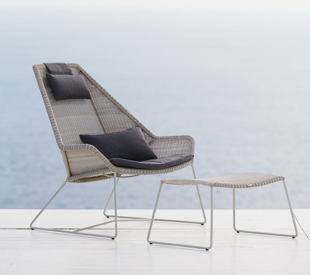 Chaise grise moderne avec coussin noir et ottoman gris devant un paysage pittoresque.
