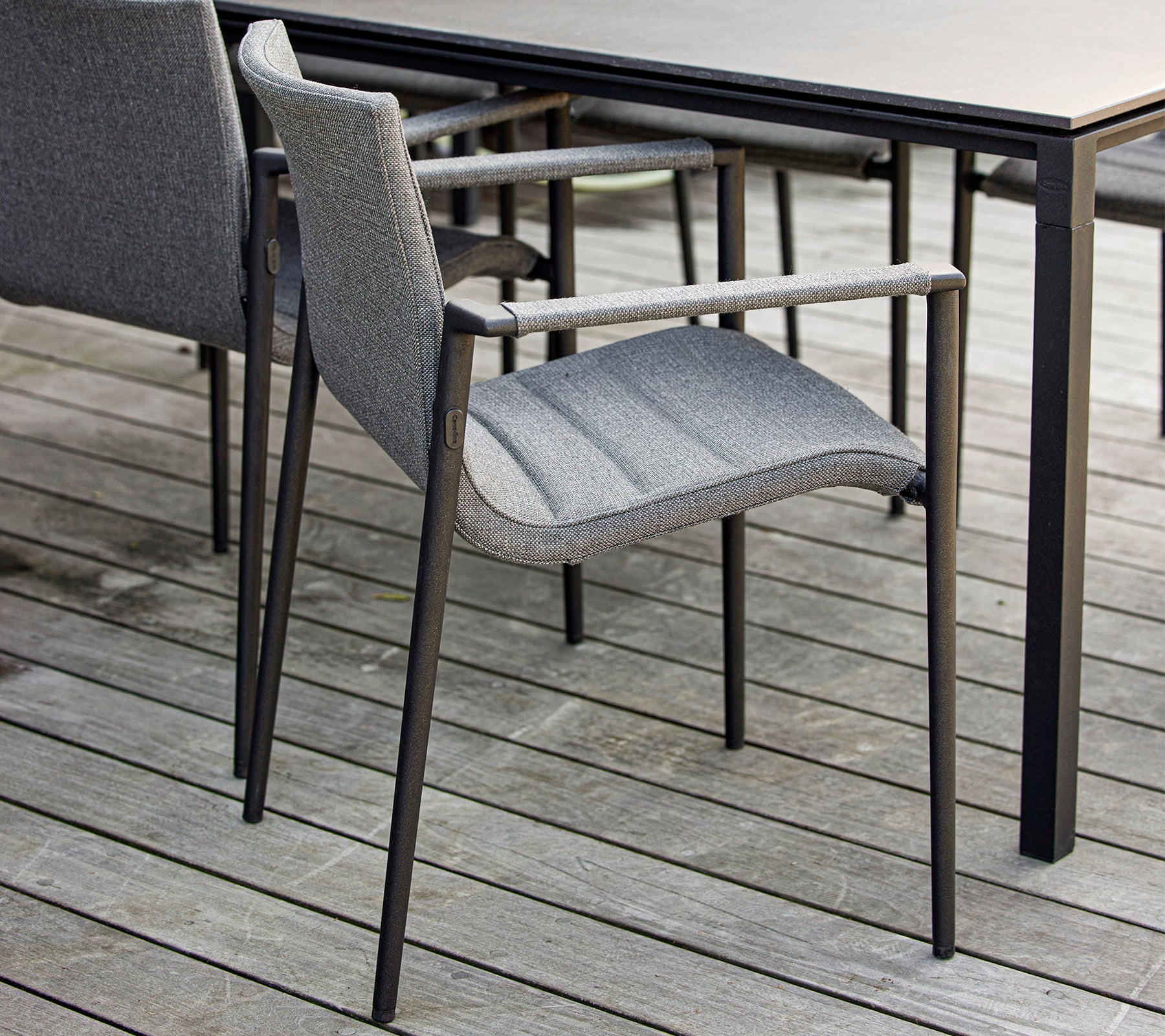 Chaise grise élégante avec accoudoirs placée à côté d'une table noire élégante sur une surface en bois. Idéale pour des environnements extérieurs modernes.