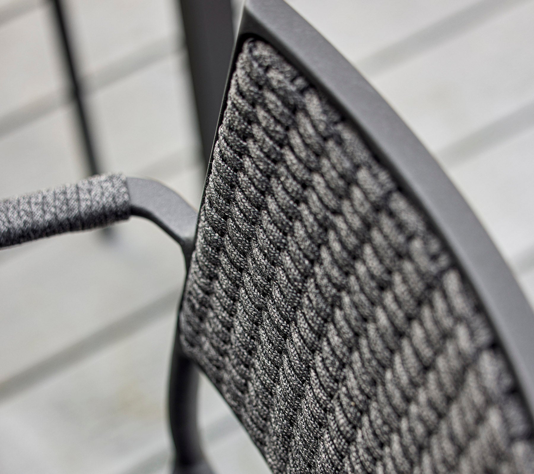 Gros plan d'un dossier de chaise présentant un design tissé texturé et un cadre en métal épuré, mettant en avant un savoir-faire moderne.