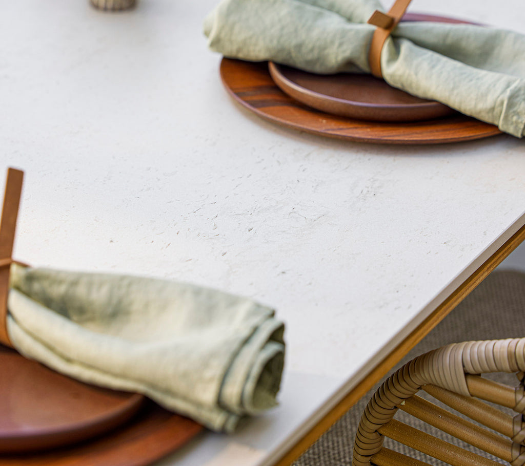 Mise en place avec des assiettes en bois et des serviettes vertes élégamment roulées, maintenues par un porte-serviette en bois, créant une atmosphère naturelle et accueillante.
